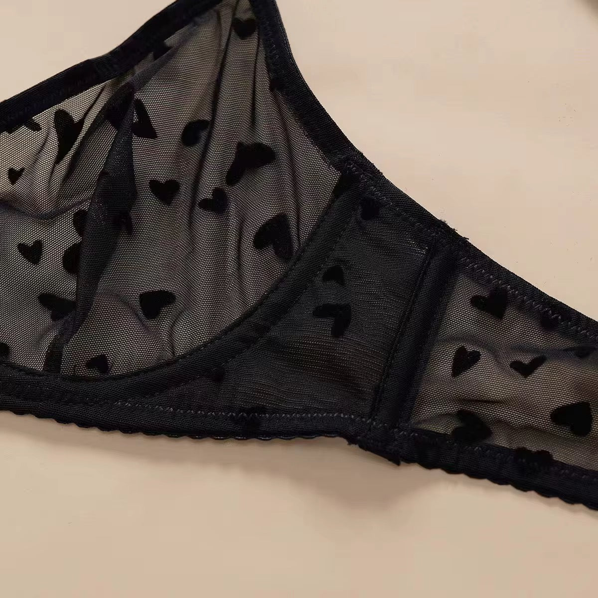 Black lace lingerie with heart patterns on a beige background