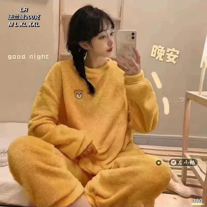 Person wearing yellow pajamas taking a mirror selfie in a room with text on the wall.
