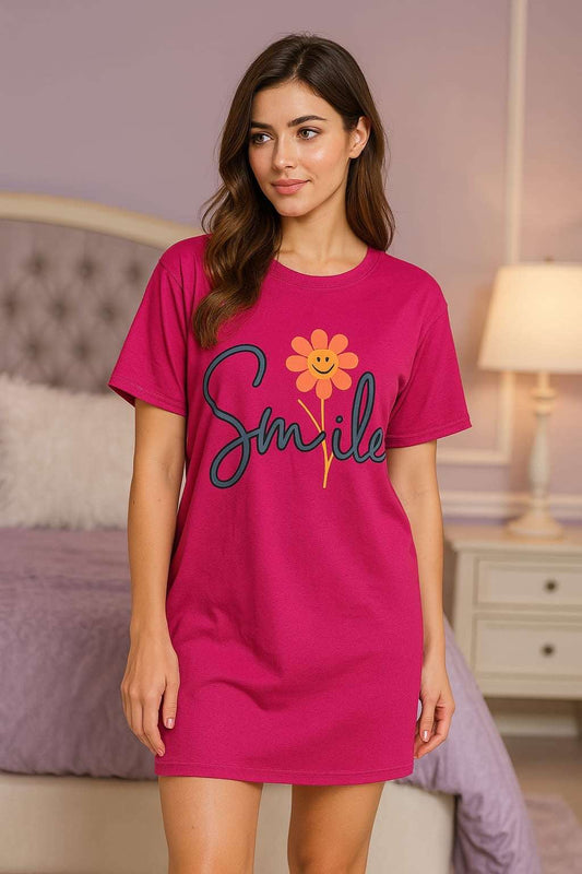 Woman wearing a pink nightshirt with 'Smile' and a flower design in a bedroom setting.