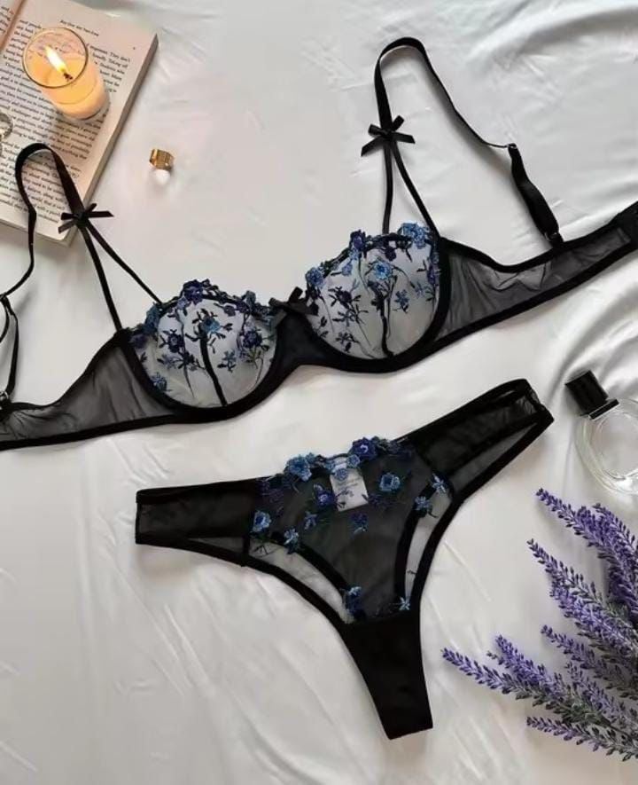 Black lingerie set with floral embroidery on a white surface, accompanied by a book and candle.