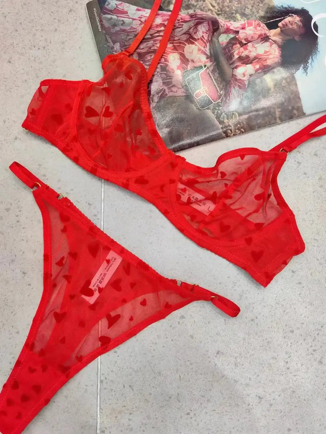 Red heart-patterned lingerie set on a light gray surface with a magazine in the background.
