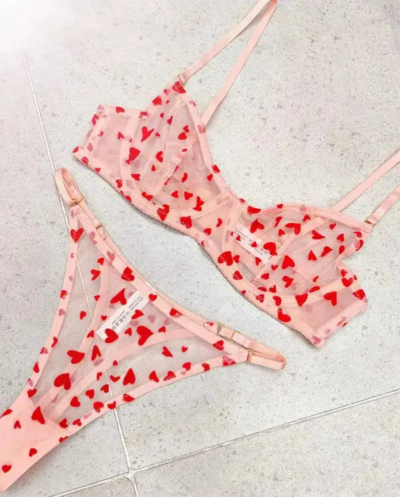 Pink lingerie set with red heart patterns on a light gray surface