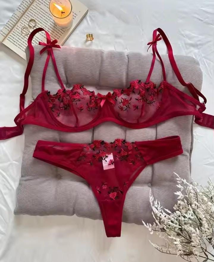 Red lingerie set with floral details on a gray cushion, surrounded by a book and candle.