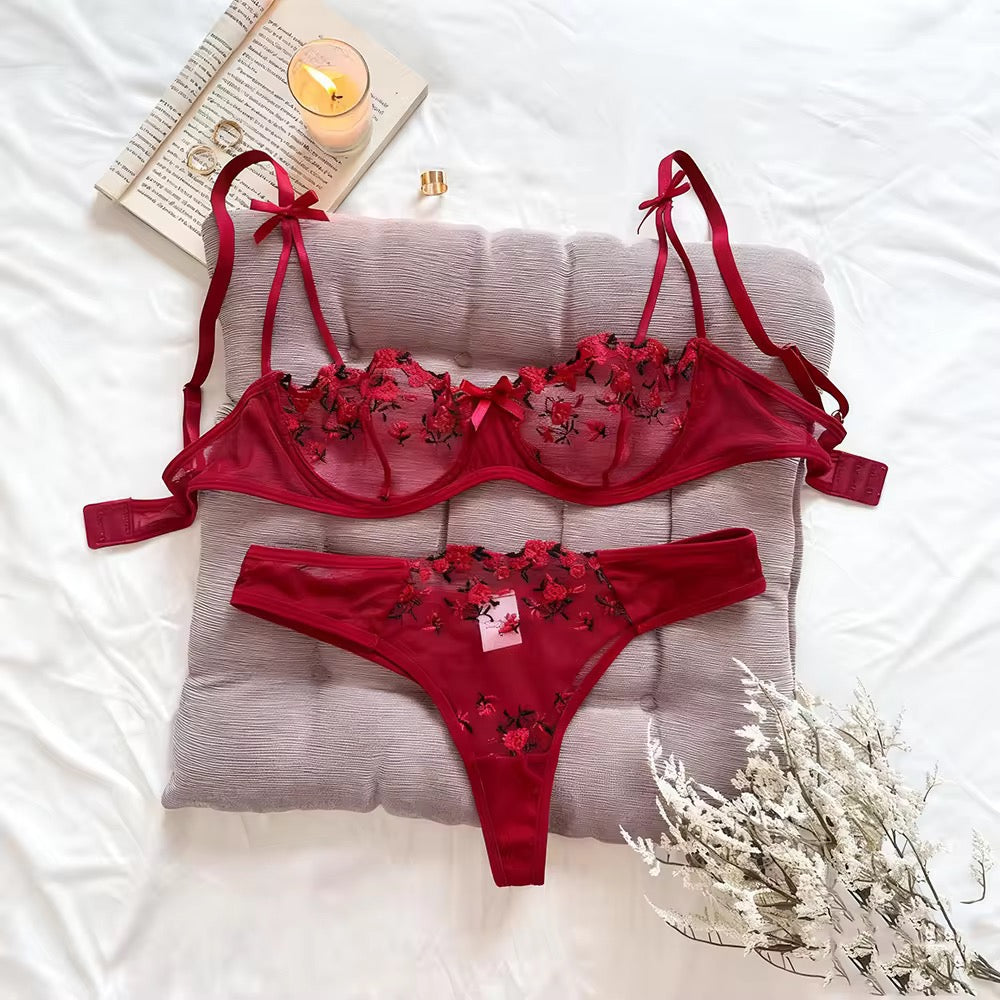 Red lingerie set with floral details on a pillow with a candle and book in the background.