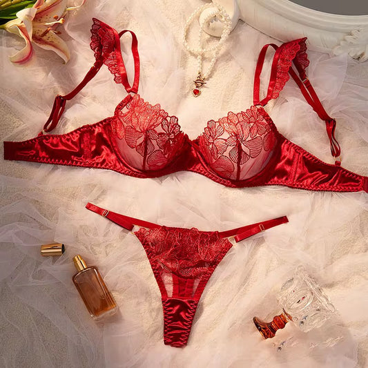 Red lace lingerie set on a textured surface with flowers and a bottle.
