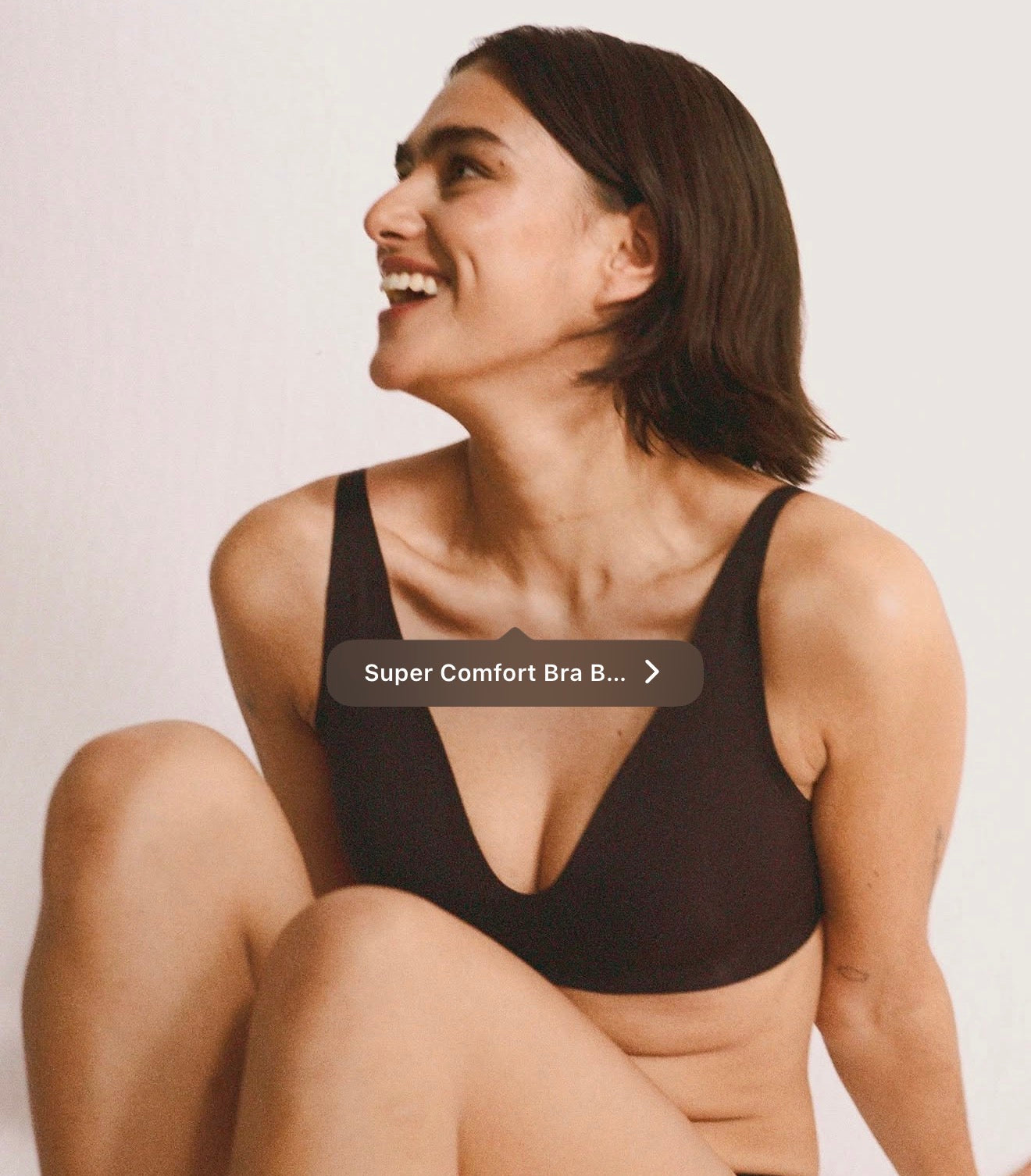 A woman wearing a dark brown or very deep black comfort bra, smiling and looking upward against a plain light background. A text overlay reads 'Super Comfort Bra B.