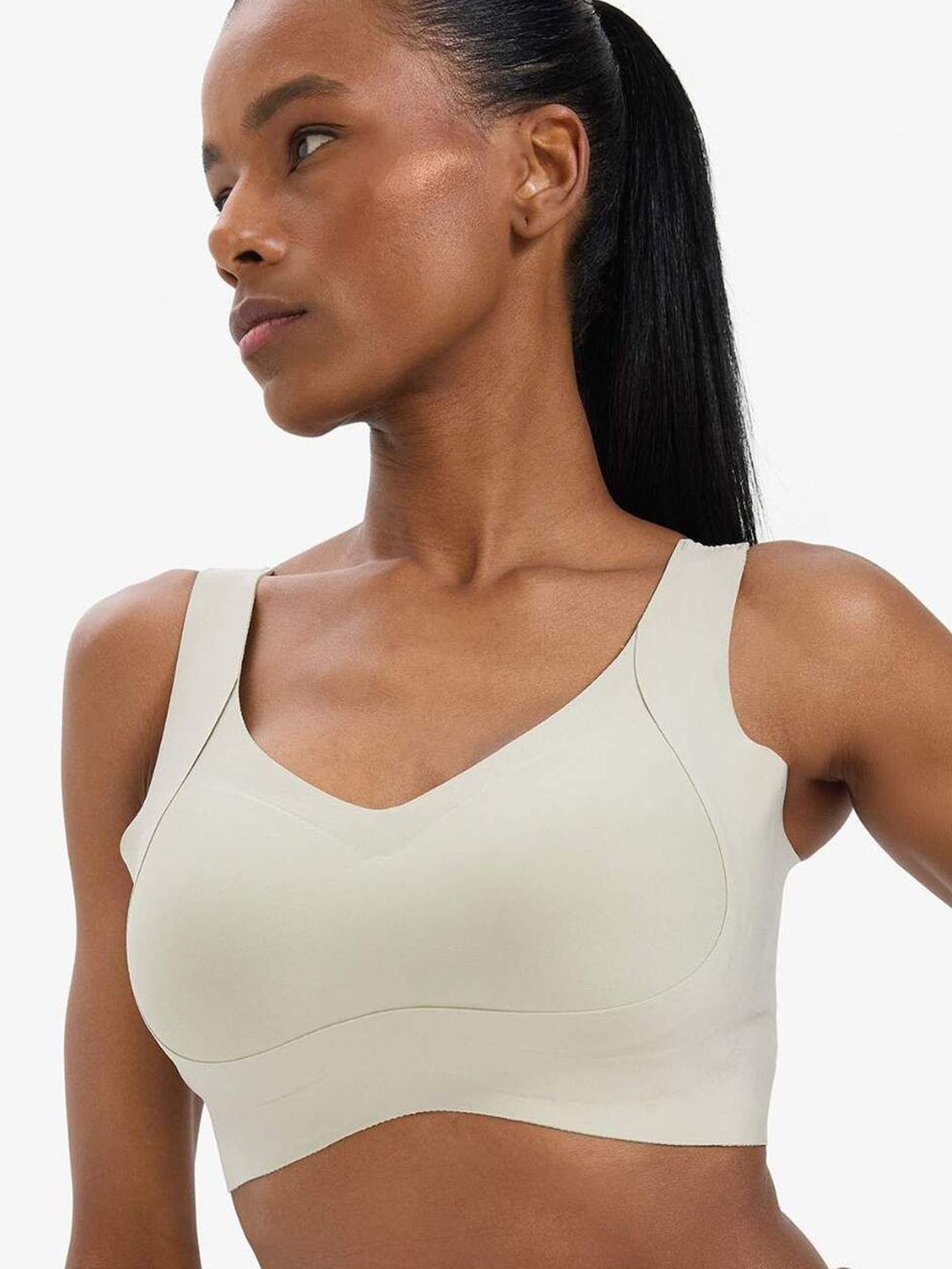 A woman wearing a light beige wireless sports bra, shown from the chest up against a clean white background.