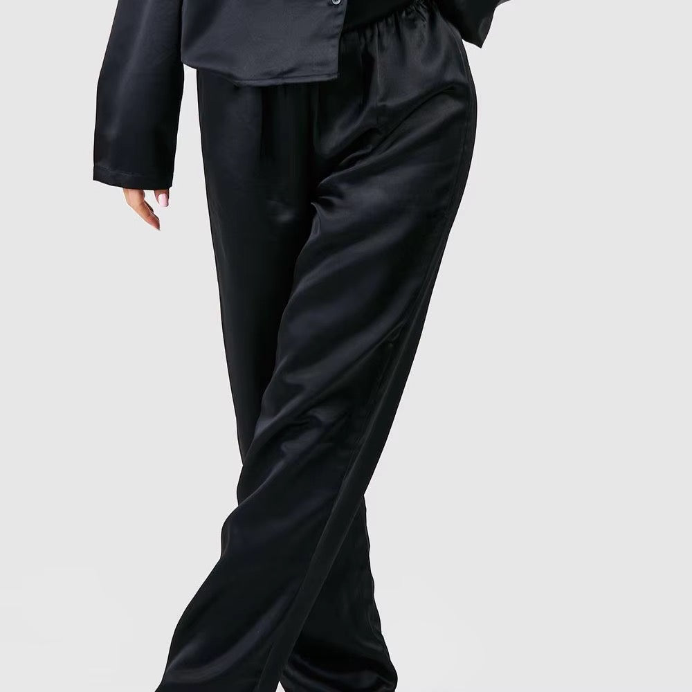 Black satin wide-leg trousers worn by a model, paired with a matching black satin blazer, shown against a light gray studio background.