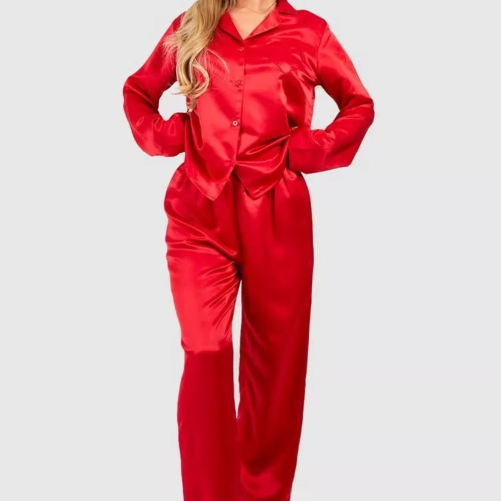 A woman wearing a shiny red satin pajama set with a long-sleeve button-front top and matching pants, shown against a plain light gray background.