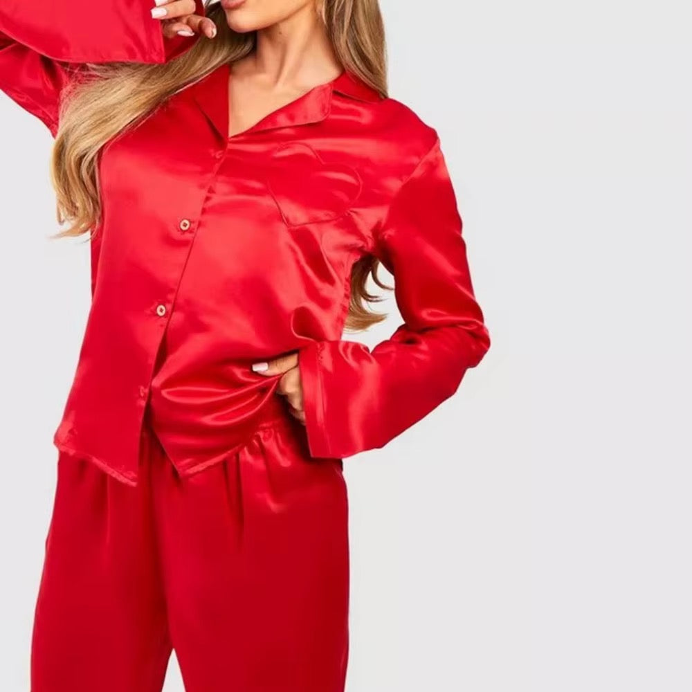 A woman wearing a shiny red satin pajama set with a long-sleeve button-front top and matching pants, photographed against a light gray studio background.