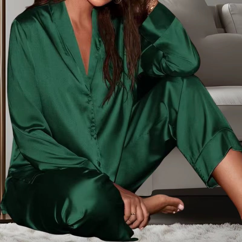 A woman wearing a silky satin pajama set in emerald green, sitting on a white shag rug in a cozy indoor setting.