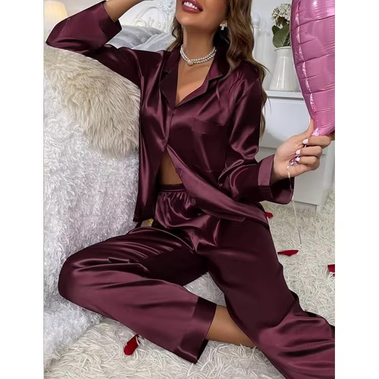 A woman wearing a satin pajama set in deep burgundy, sitting on a white shag rug and holding a pink pillow.
