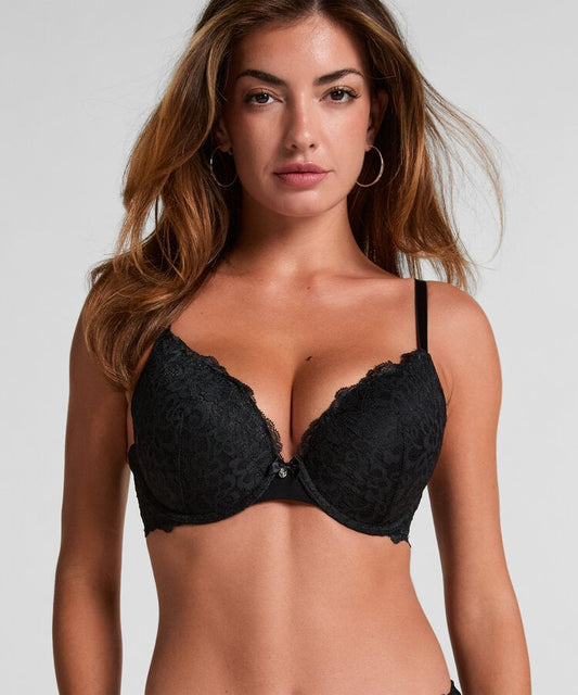 A woman modeling a black lace underwire bra against a light gray studio background.