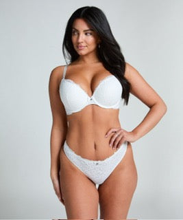 A woman modeling a white two-piece lingerie set consisting of a bra and matching lace panties against a light gray studio background.