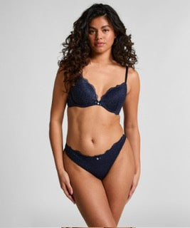 A woman modeling a dark navy blue lace lingerie set against a light gray studio background.