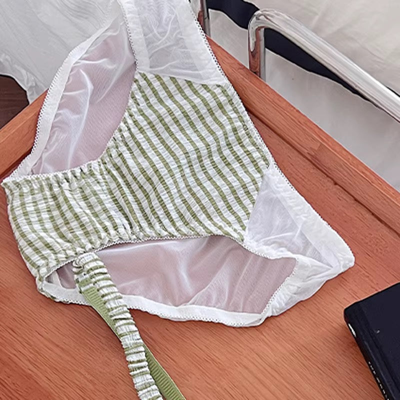 A green and white striped bralette with white mesh trim and a matching striped tie strap, laid flat on a wooden table.