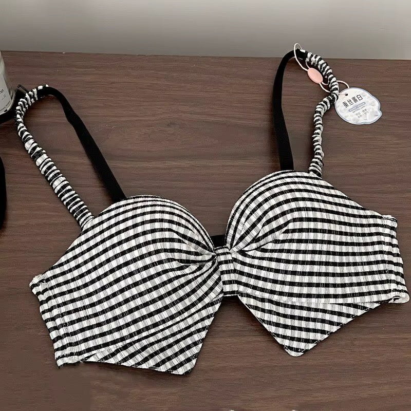 A black and white gingham check bikini top with a large front bow and patterned shoulder straps, laid flat on a dark wood surface with a product tag attached.