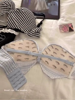 A beige underwire bra with a small leaf pattern, laid flat on a white bed alongside other bras and a black-and-white striped pillow.