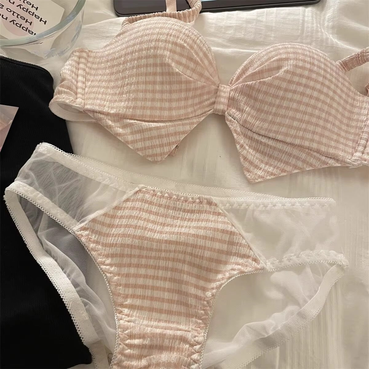 A two-piece women's underwear set featuring a bow-front bra and matching lace-trim briefs in a soft beige and white gingham pattern, laid flat on a white textured surface.