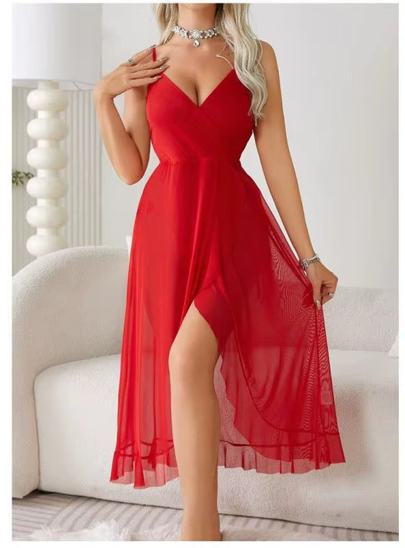 A woman wearing a bright red sleeveless midi dress with a V-neckline, fitted bodice, and flowing sheer overlay skirt, posed in front of a white sofa in a bright indoor setting.