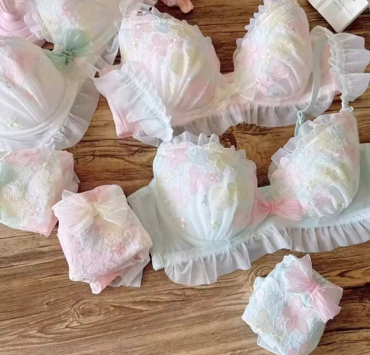 A collection of pastel pink and white floral lace lingerie sets, including bras and matching panties, arranged on a wooden surface.