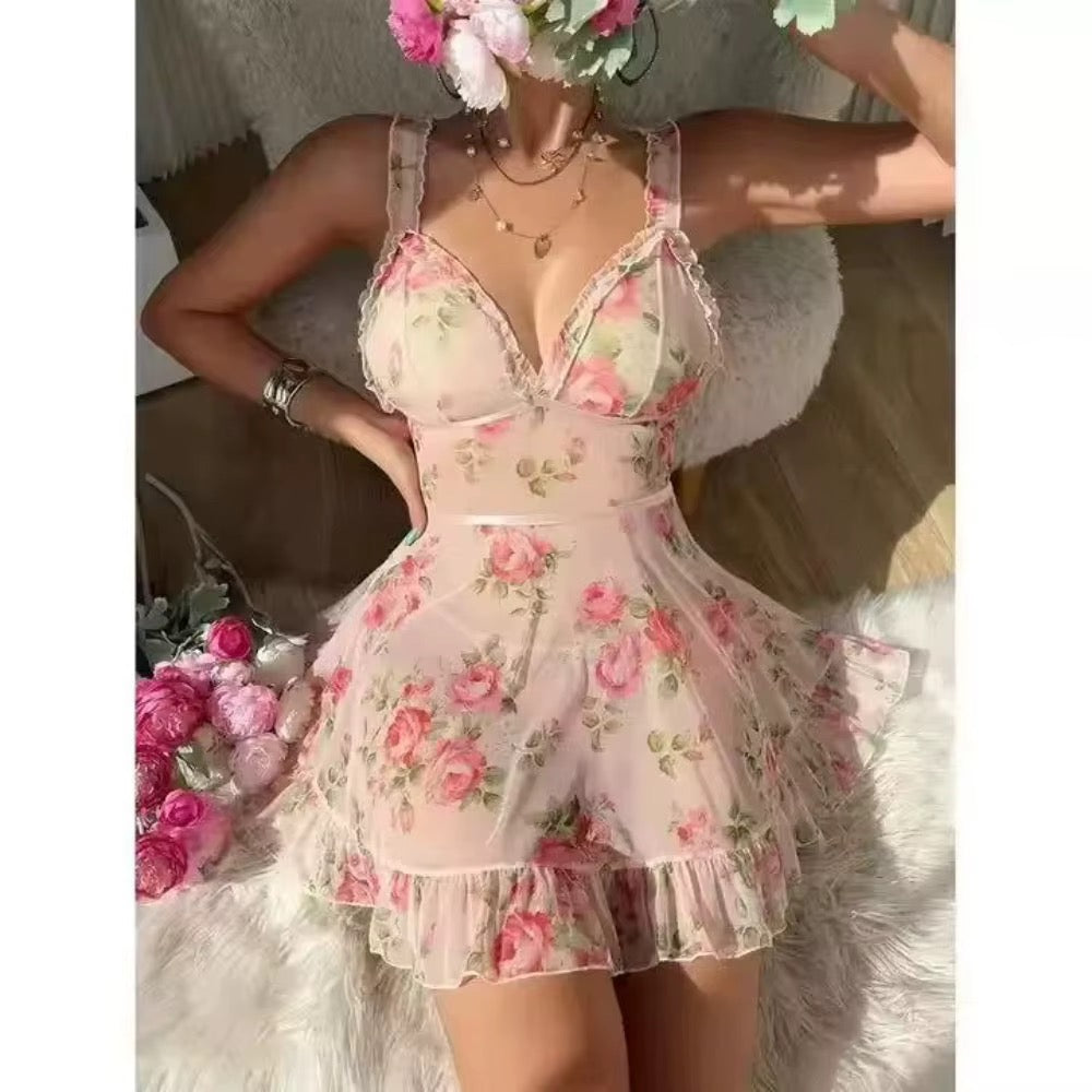 A woman wearing a sheer pink tulle mini dress with a pink and green rose floral print, posing on a white faux fur rug with flowers.