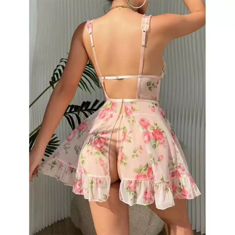 A woman shown from the back wearing a sheer light pink lingerie chemise with a pink and green floral print, featuring thin straps, a low open back, and a ruffled skirt.