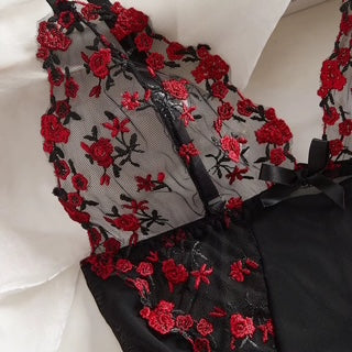 Black lace lingerie with red floral embroidery and sheer mesh cups, laid flat on a white fabric background.