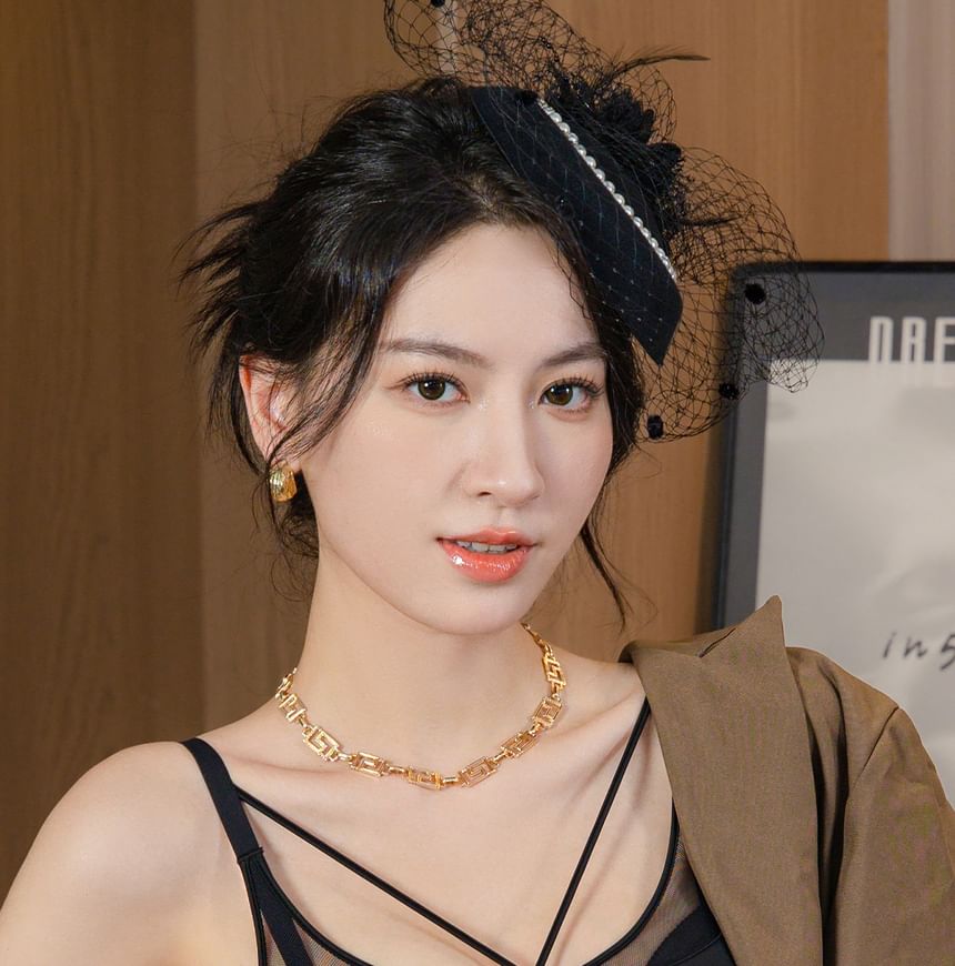 Woman wearing a black headpiece and gold necklace indoors