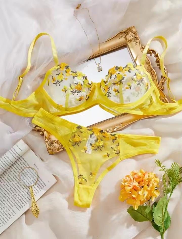 Yellow floral lingerie set on a white surface with a gold frame and flowers.